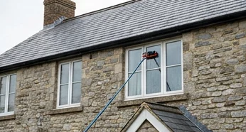 Illustrative water-fed brush washing a window on a grey stone house