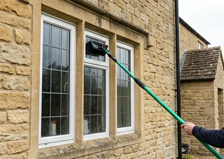 Illustrative water-fed brush cleaning white casement windows on a stone house